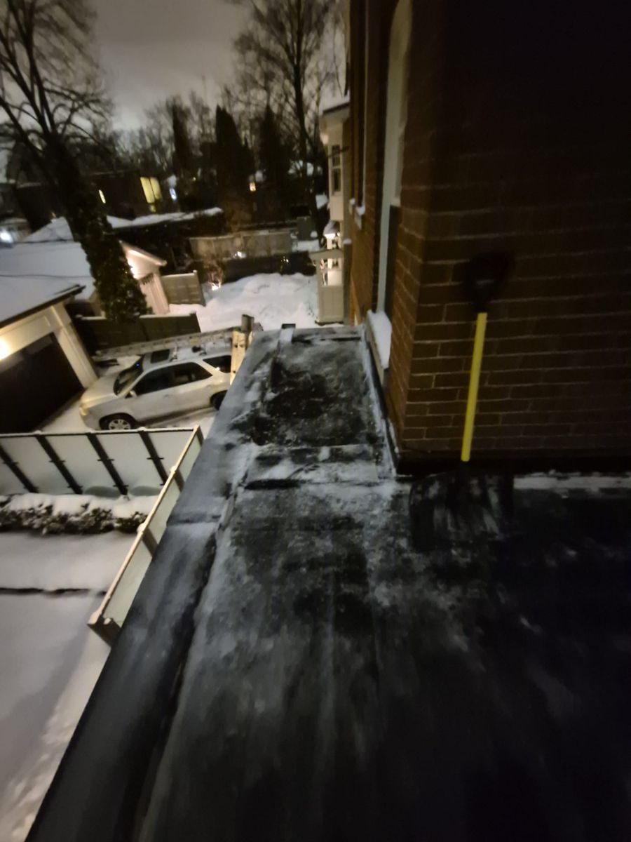 Snow shovel on a narrow roof ledge cleared next to a brick wall
